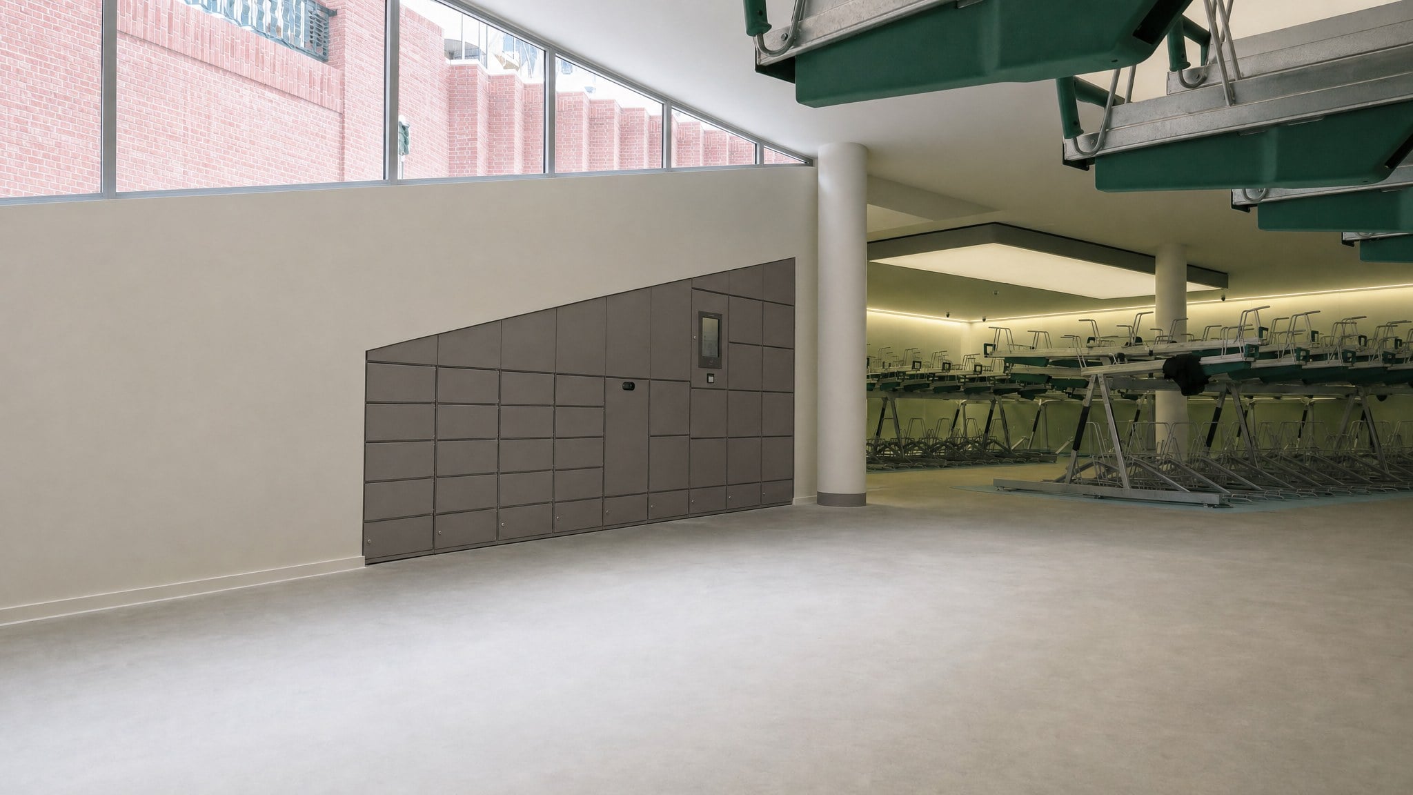 Angular bank of gray lockers with display and access panel in an empty room.