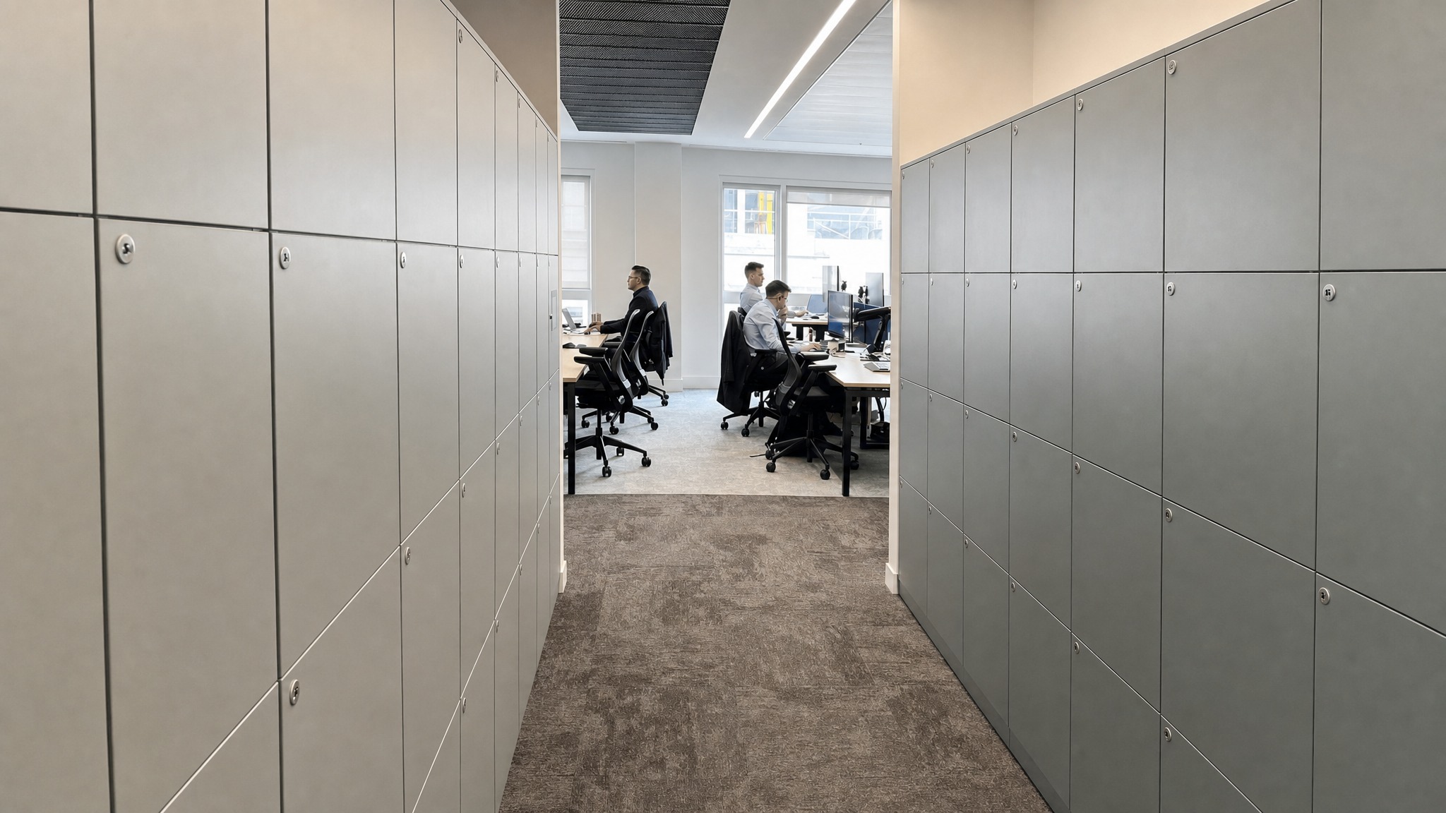 Gray locker banks along both sides of a hallway leading to an open office area.
