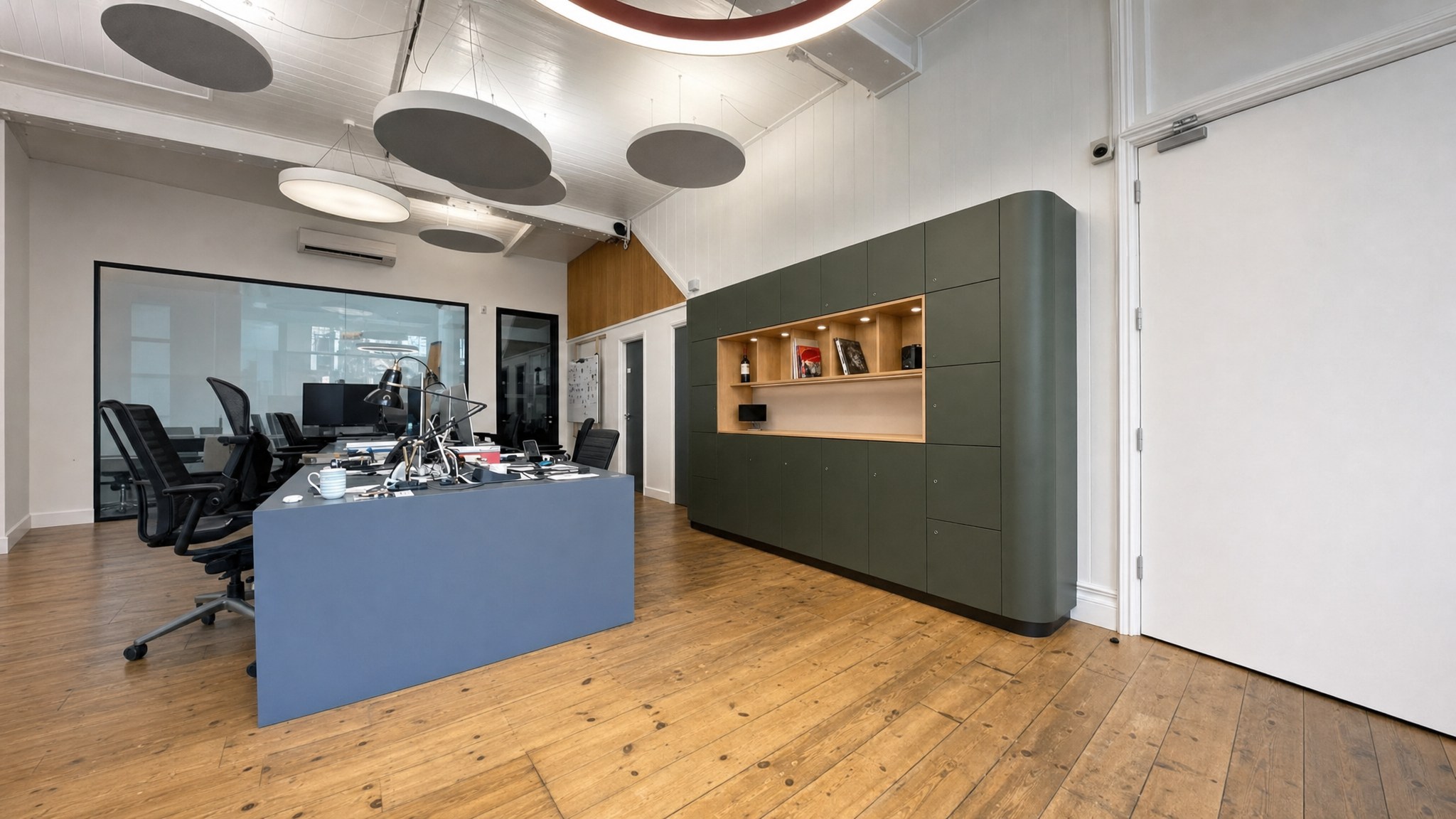 Wall of dark green lockers with open shelving in a modern office with wood flooring.