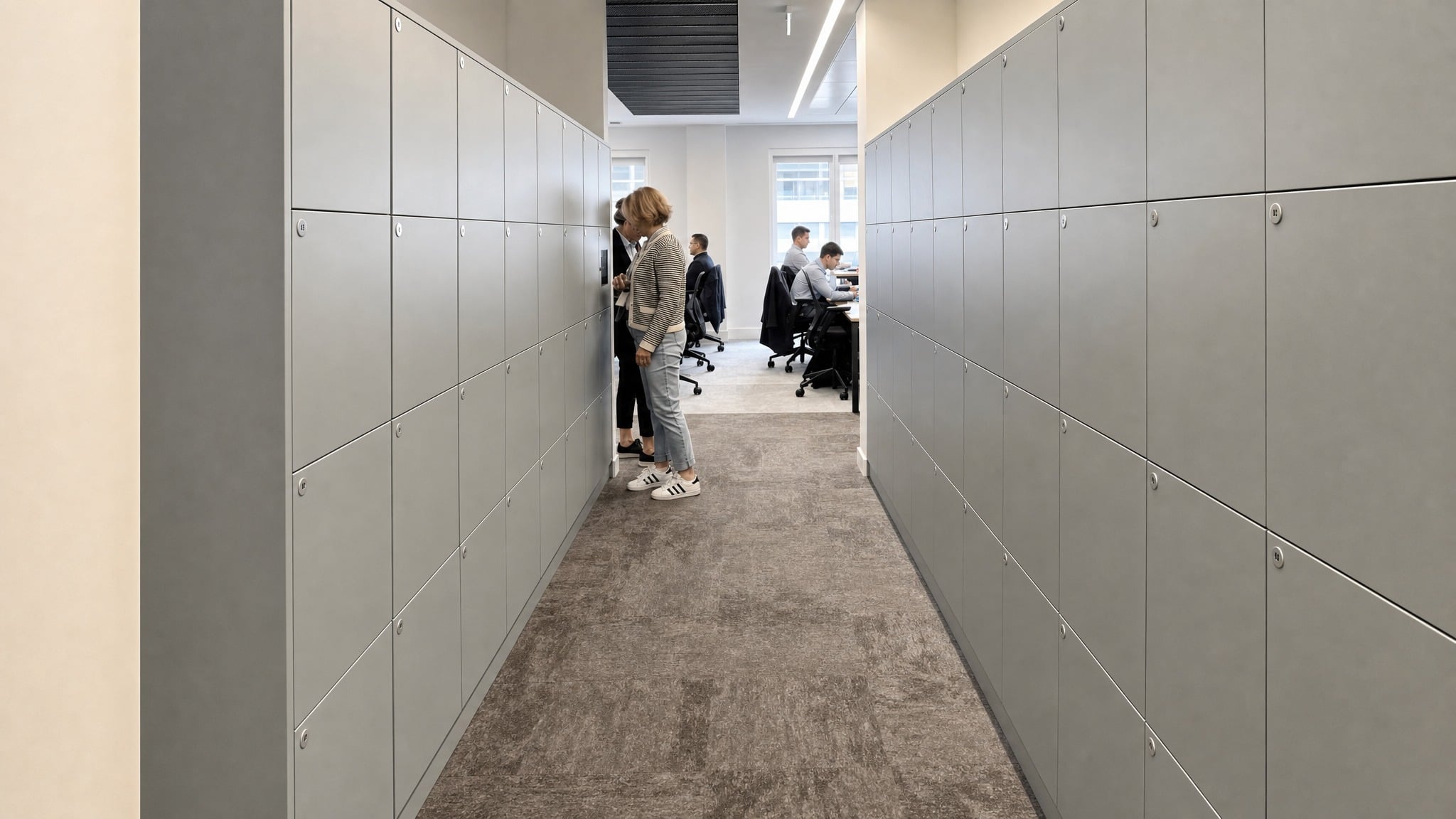 Gray locker banks lining both sides of a hallway with people working at desks beyond.