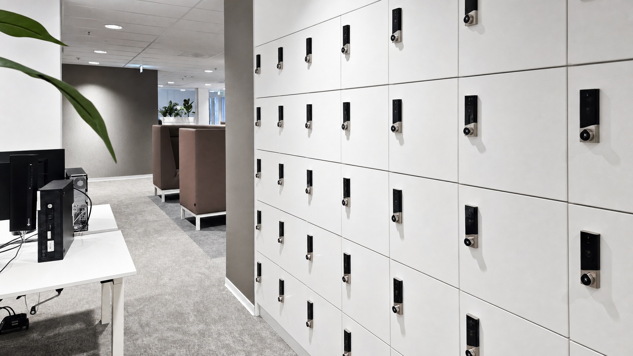 Wall of white lockers with black electronic locks in a carpeted office area.
