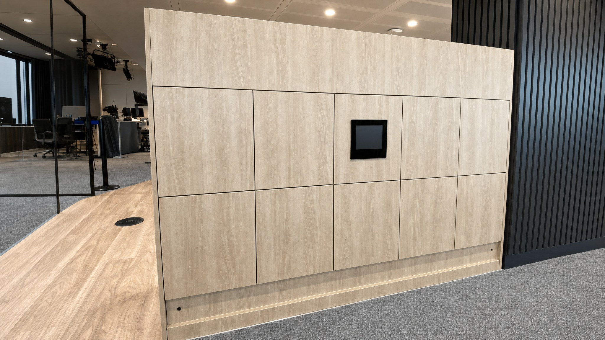 Wood-finish locker bank with a central dark display in a modern office interior.