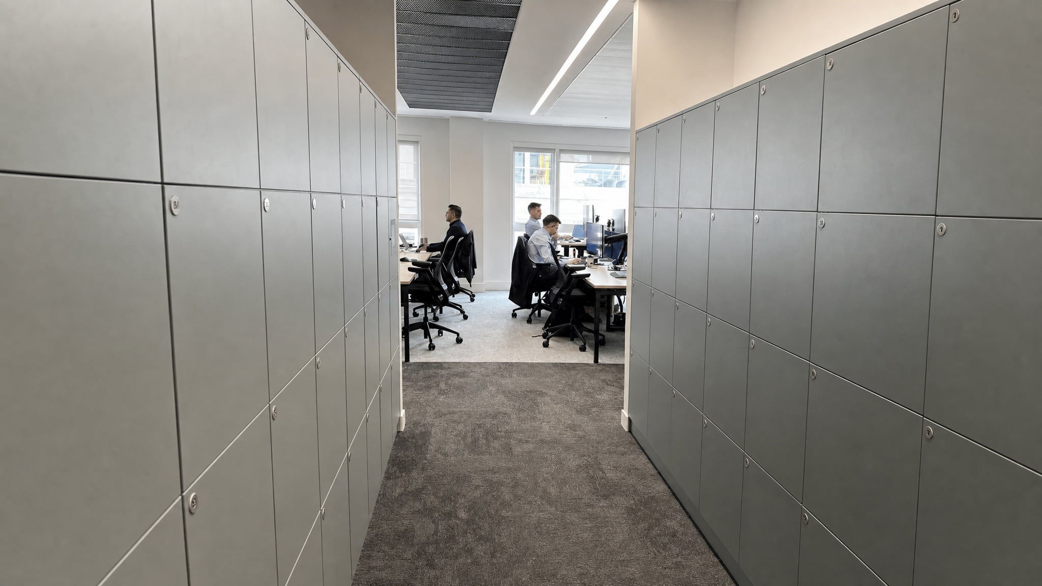 Two rows of gray lockers lining a corridor leading to an open office area.