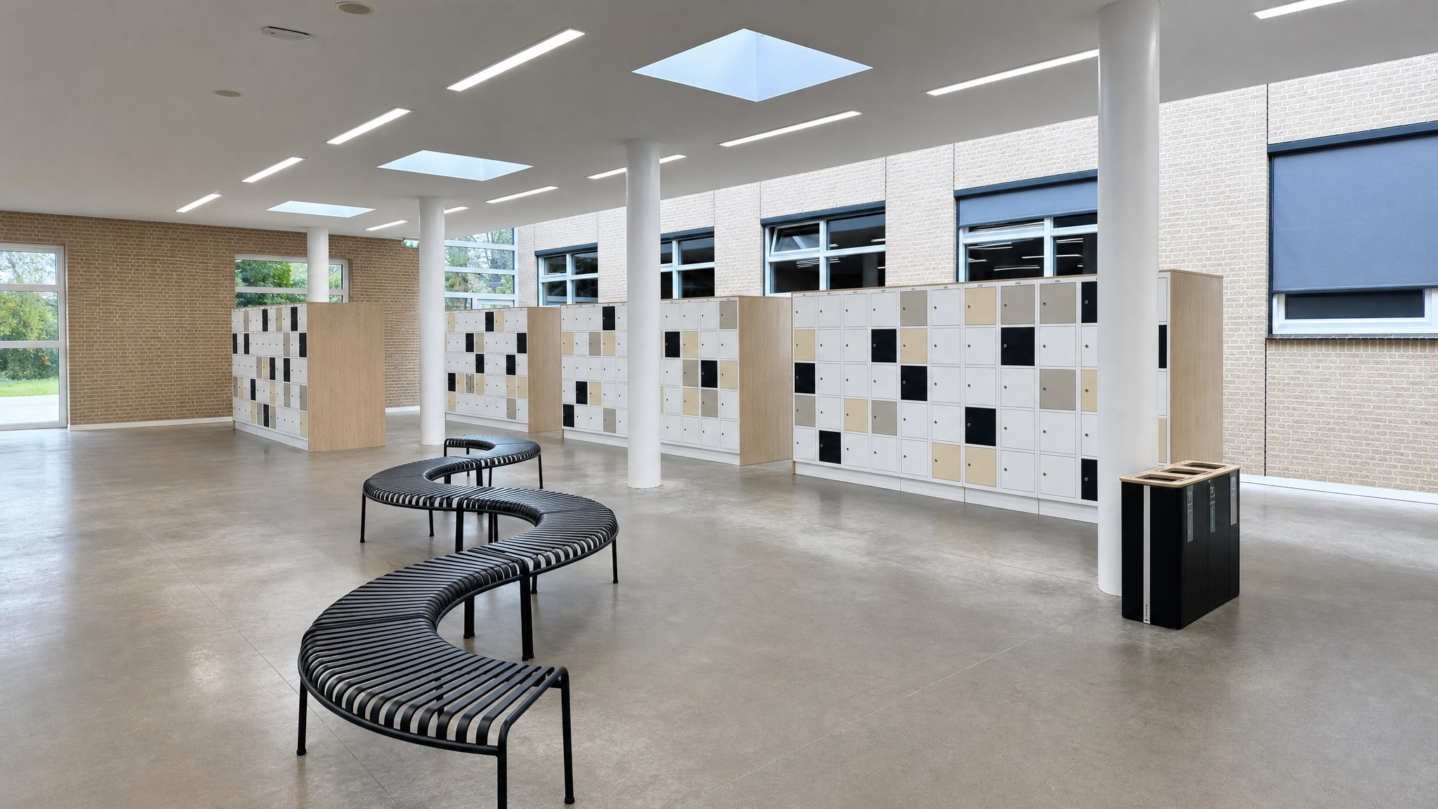 Room with light wood lockers and black, beige, and white locker doors beside curved benches.