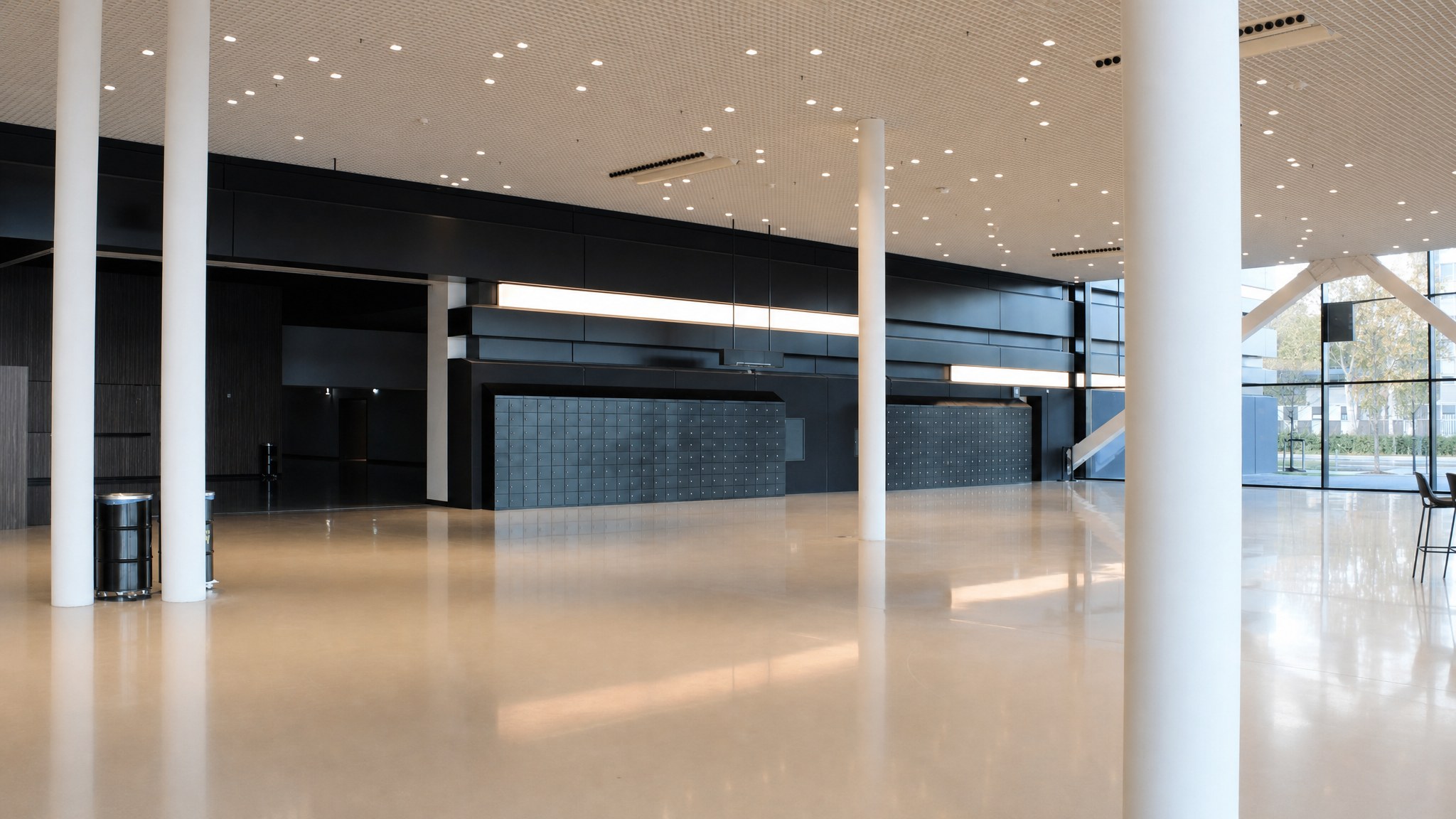 Two large walls of dark lockers in a spacious modern lobby with columns and polished floor.