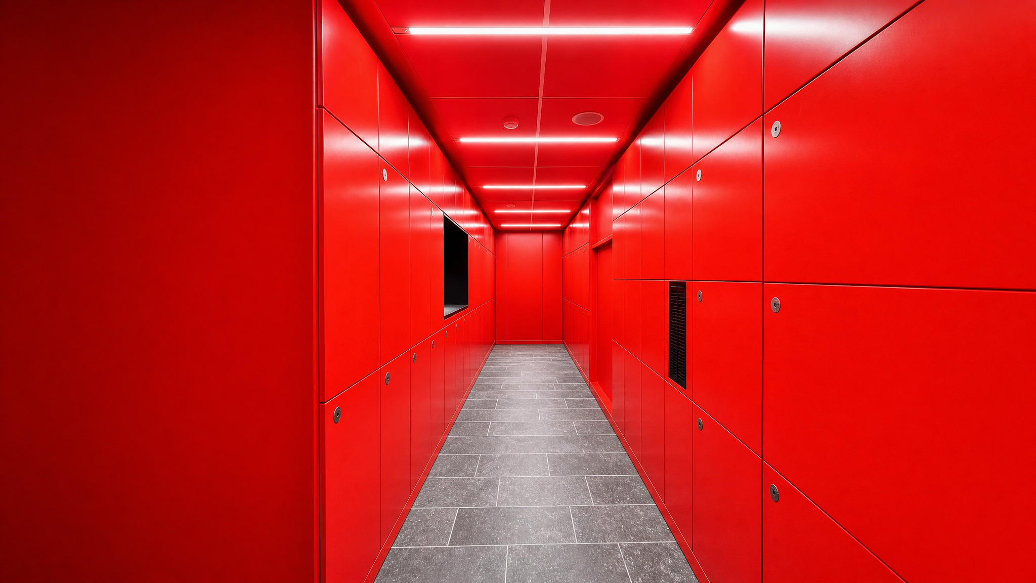 Hallway of red smart parcel lockers with gray tile floor and ceiling lights