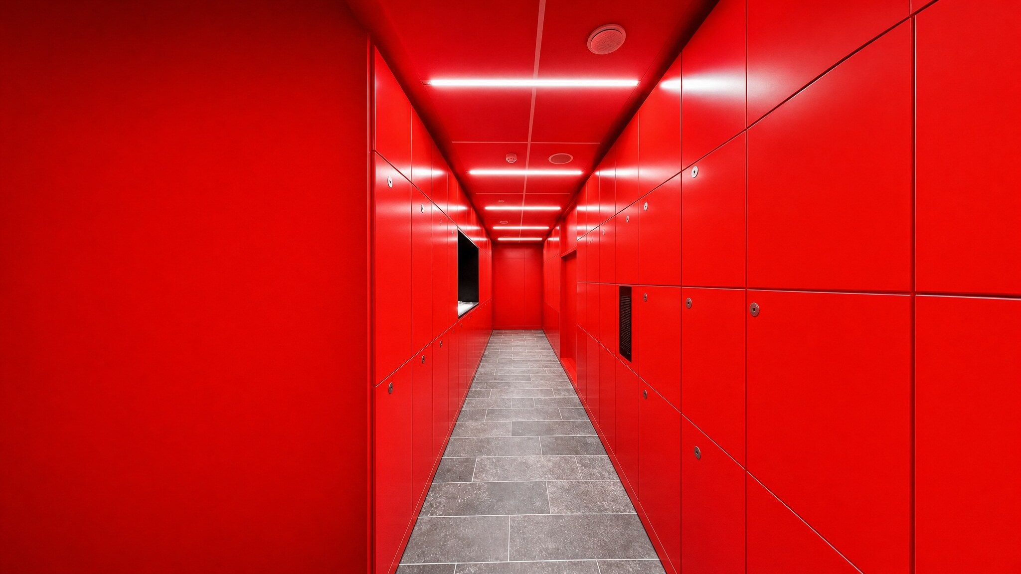 Long hallway lined with bright red locker banks and tiled floor.
