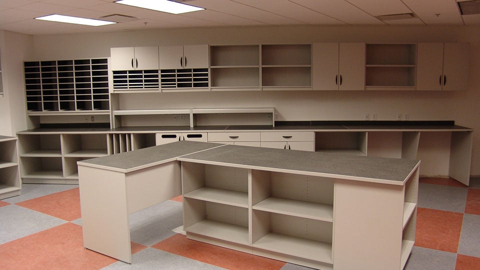 Custom modular casework with mail slots, storage cabinets, and U-shaped work surfaces designed for centralized mailrooms or corporate support areas.